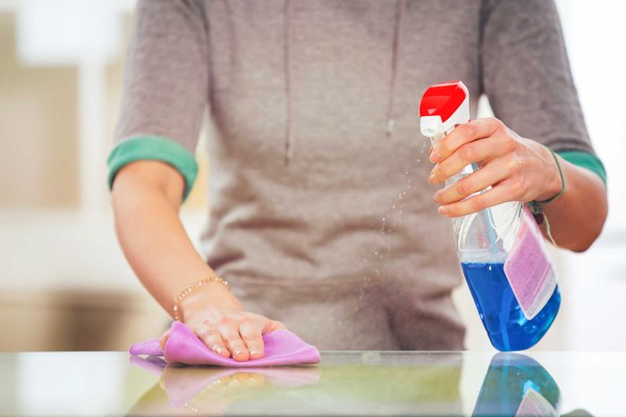woman cleaning a countertop with cloth and spray bottle