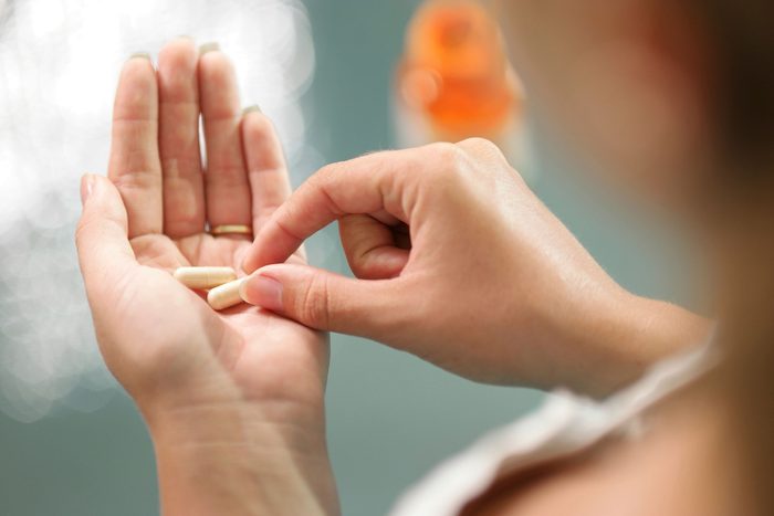 woman grabbing one of two pills from her palm