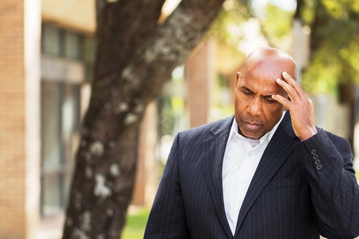 Man in a suit outside holding his head as if having a headache.