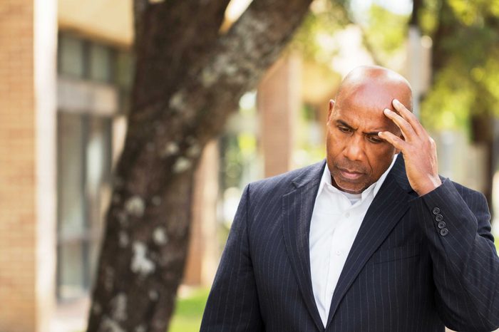Man in a suit outside holding his head as if having a headache.