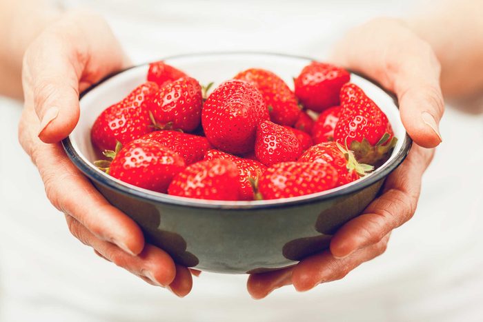 hands holding a bowl of strawberries