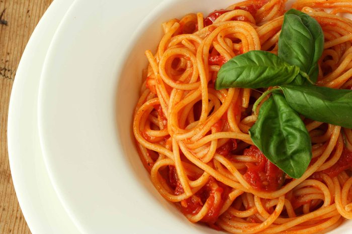 White bowl of tomato pasta with basil.