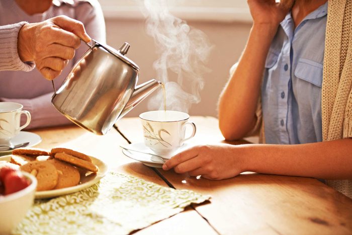 woman pouring another woman a cup of tea with teapot