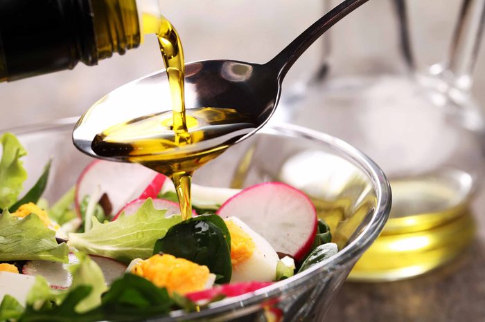 Spoonful of olive oil being poured onto a bowl of salad.