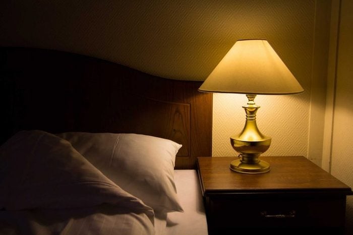 A lit lamp on a nightstand in a dark bedroom.