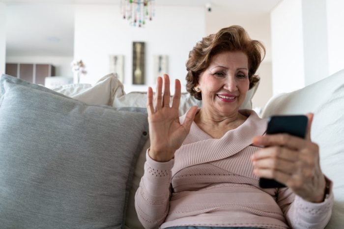 senior woman sitting on couch at home on a video call with family and friends