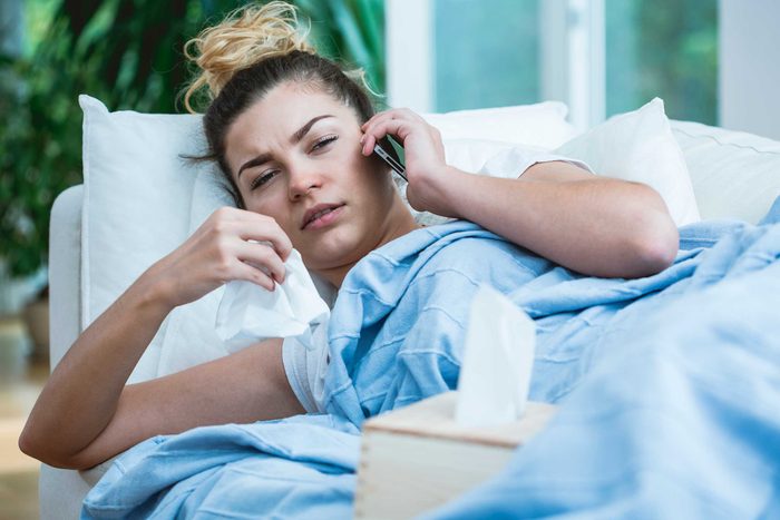 Sick woman in bed, talking on her phone and holding a tissue.
