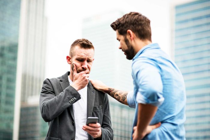 worried man looking at phone, another man with hand on his shoulder