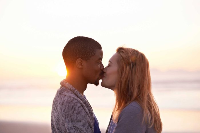 man and a woman kissing on a beach at sunset