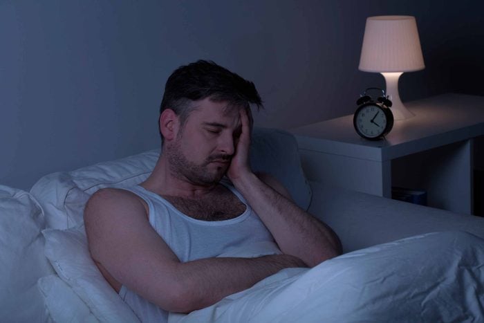 man sitting up in bed at night, holding his head