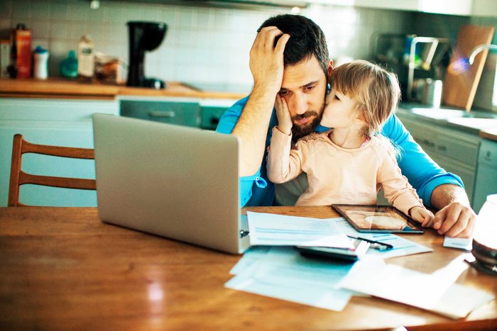 stressed father in front of computer, daughter in lap kissing him