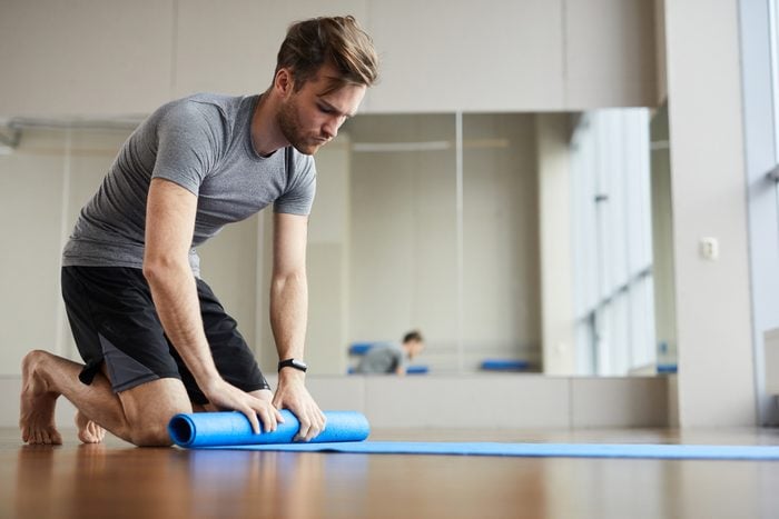 young man rolling out yoga mat in yoga studio
