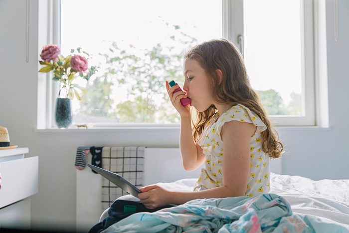young girl sitting in bedroom using inhaler for asthma