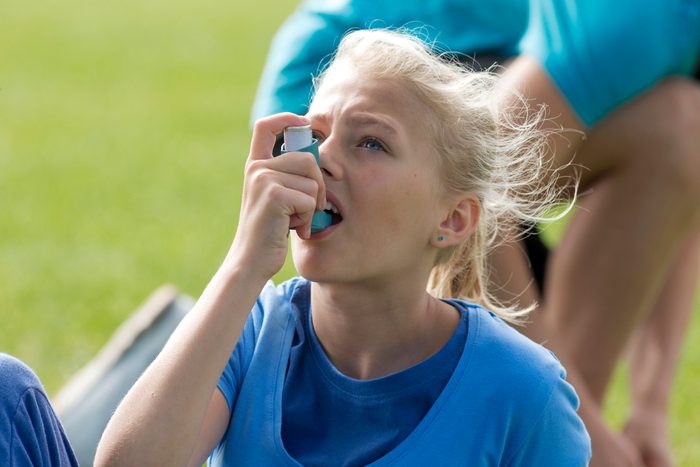 young girl using inhaler while playing sports outside