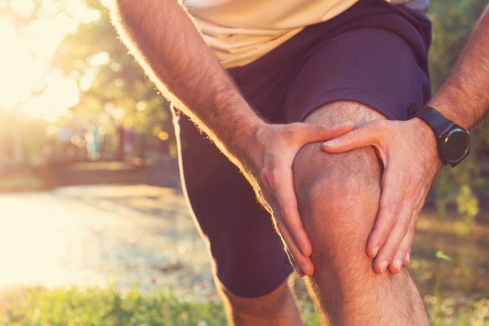 Man in shorts holding his knee as if having knee pain.