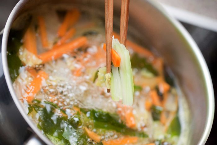 chopsticks taking vegetables out of a boiling pot