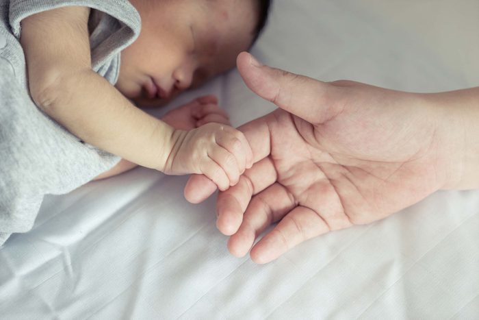 newborn baby holding adult's finger