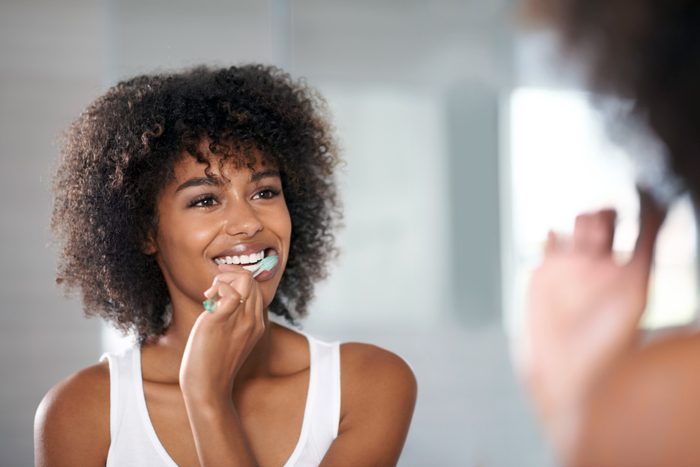 woman brushing her teeth in front of mirror