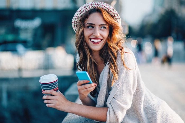 smiling woman with to-go coffee and phone
