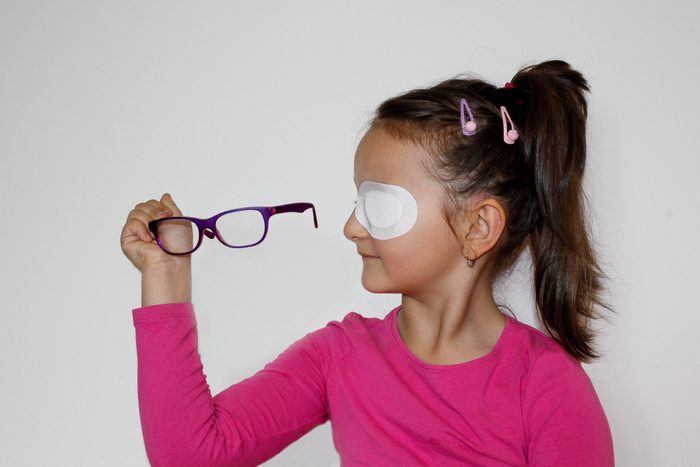 young girl with eye patch holding eyeglasses