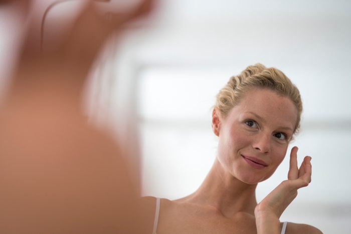 woman looking in mirror applying skin care on face