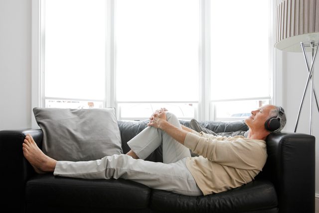 man laying on couch listening to music or podcast in headphones