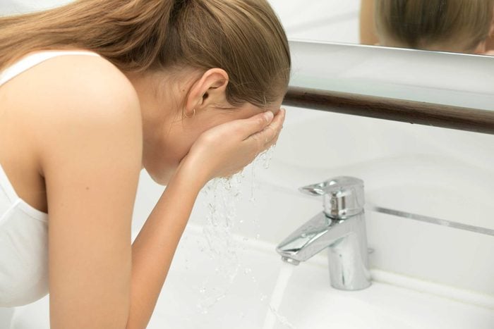 woman washing her face over a sink