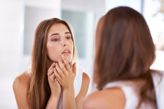 Woman looking in the mirror at a spot on her chin.