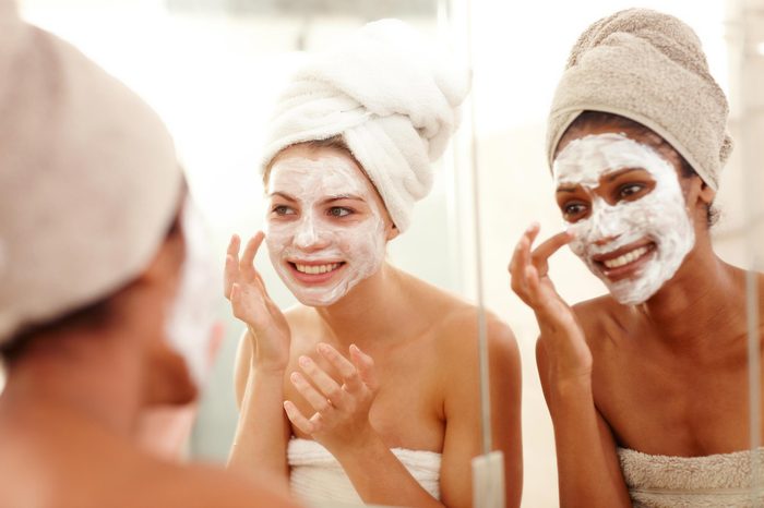 Two women wearing white skin masks looking in the mirror.