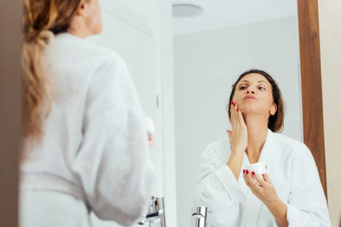 Woman applying face cream in mirror