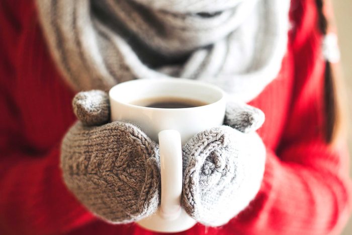 bundled up person with wool mittens holding a mug