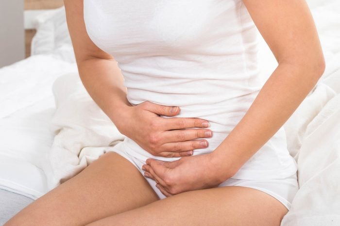 woman sitting on bed clutching stomach, in discomfort