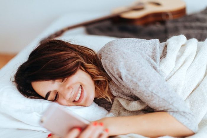 woman smiling and checking her phone in bed