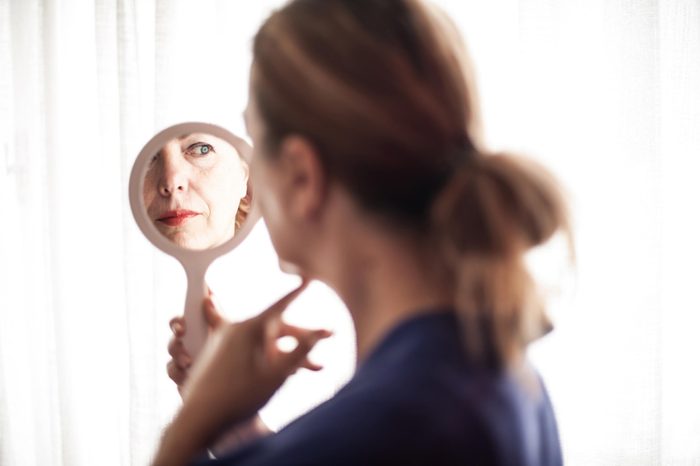 Woman looking in a hand mirror at her face.
