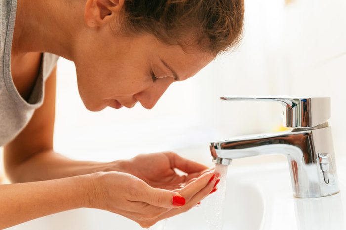 Woman washing her face with tap water in the sink.