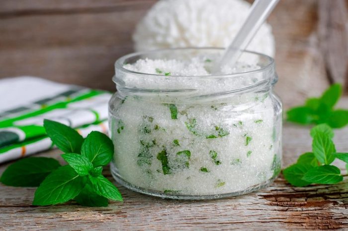 DIY mint salt scrub on a wooden surface with mint leaves around it.