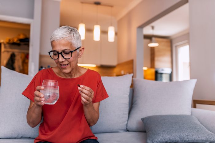 mature woman taking medication with glass of water at home