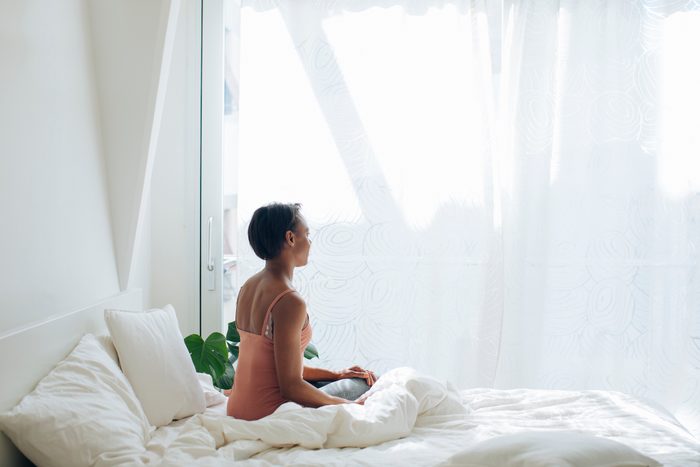 woman sitting on bed looking out window