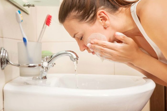 woman washing face at white sink
