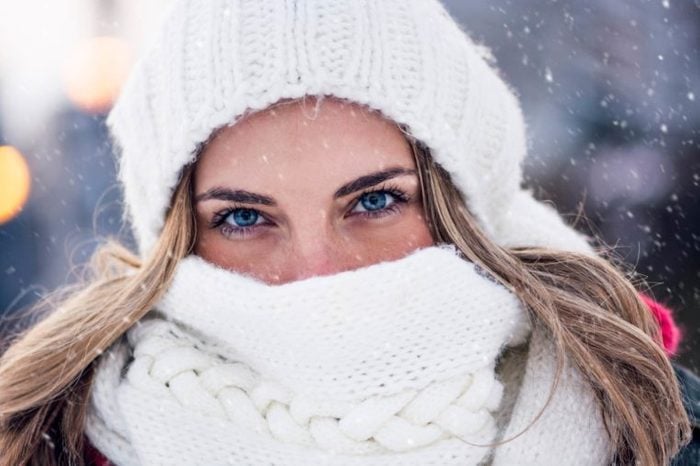 woman with blue eyes outdoors, bundled up in white hat and scarf