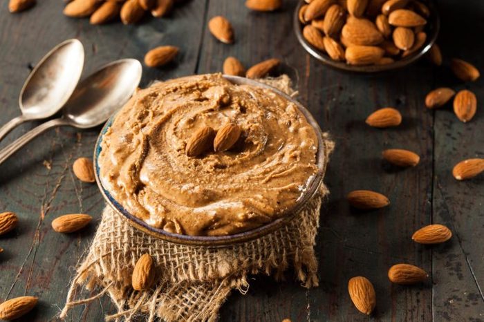 Almond butter in a bowl on a table with scattered whole almonds