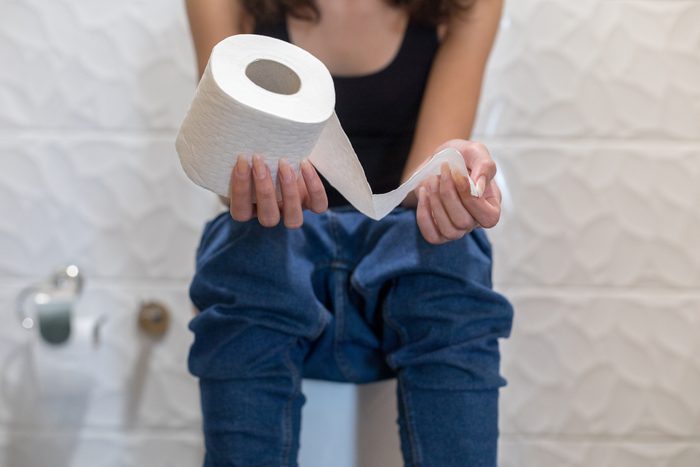 woman sitting on the toilet holding a roll of toilet paper