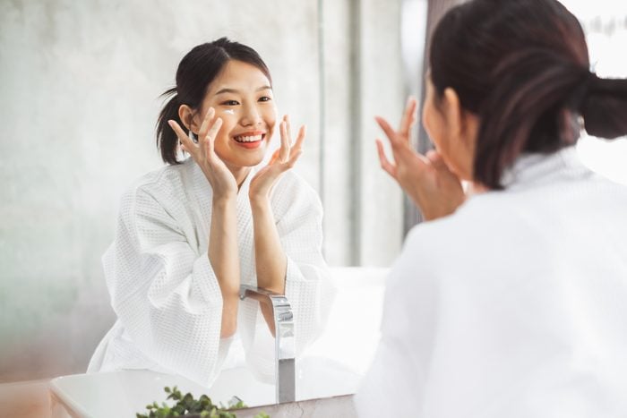 woman moisturizing face while looking in mirror