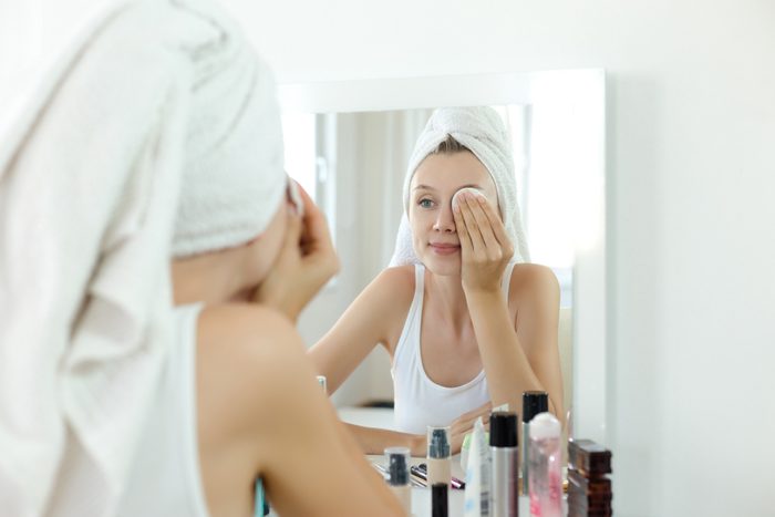 young woman cleaning her face in mirror