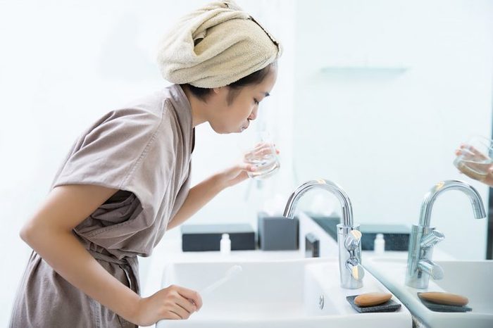 woman in robe gargling over a sink