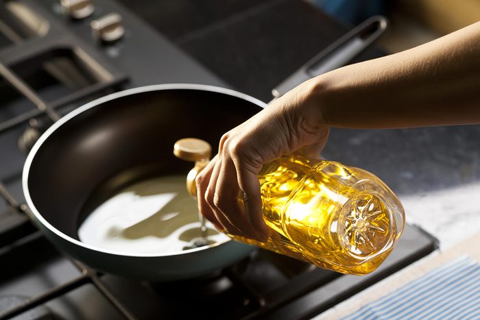woman pouring olive oil in a skillet on a stove