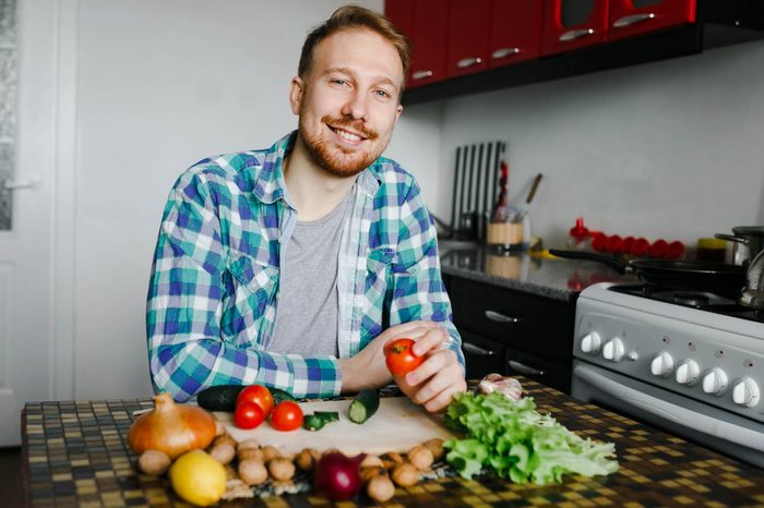 man in kitchen with fresh vegetables on and around a chopping board