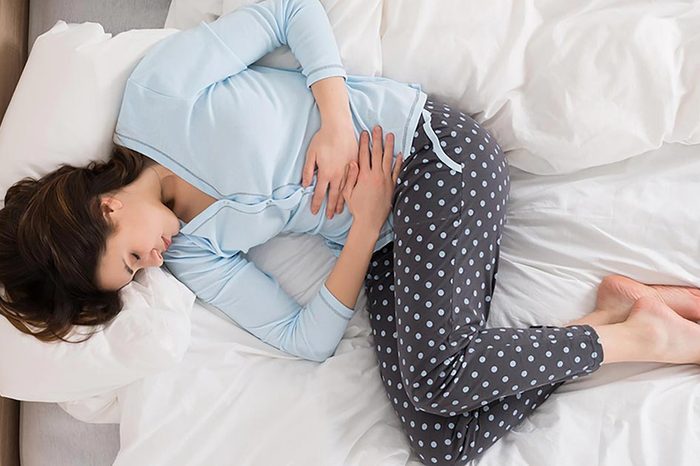 woman in bed on her side holding stomach