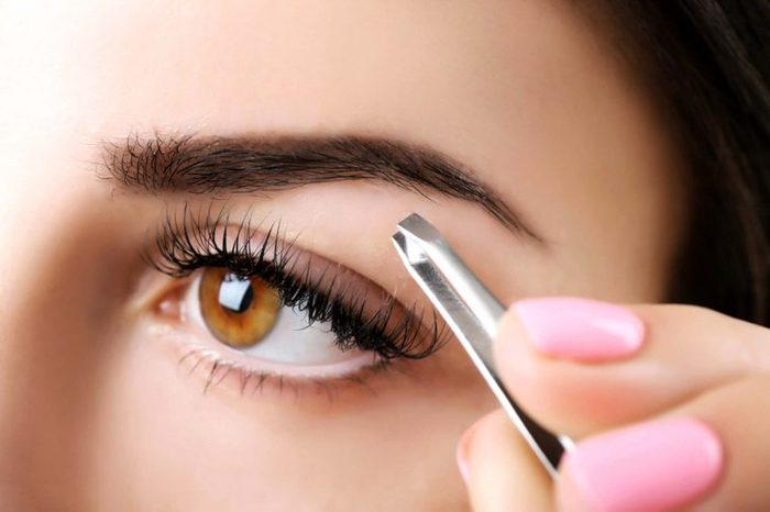 close up of a woman using a tweezer to pluck her eyebrows