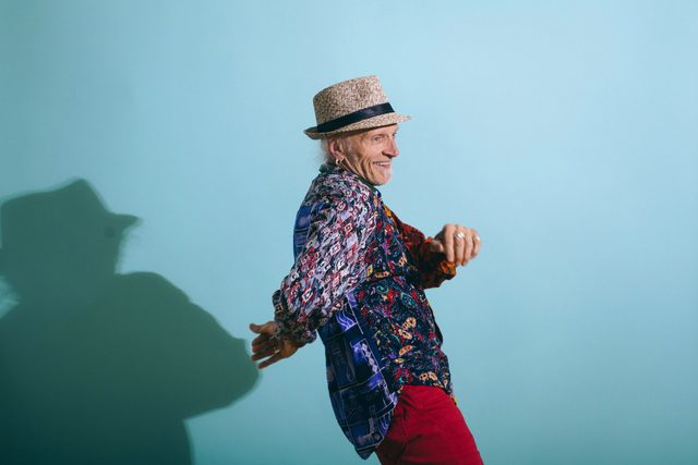senior man laughing and dancing on blue background